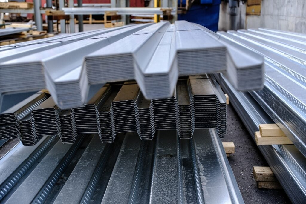 Stacks of corrugated metal decking sheets in an industrial fabrication setting.